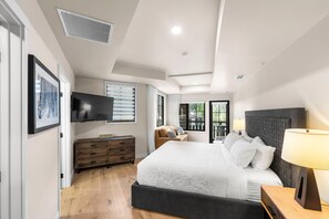 Une chambre moderne avec un grand lit, un téléviseur fixé au mur, une commode et une fenêtre avec des stores.