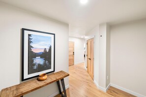 Un pasillo con piso de madera, un cuadro enmarcado en la pared y un banco de madera con una pequeña maceta.