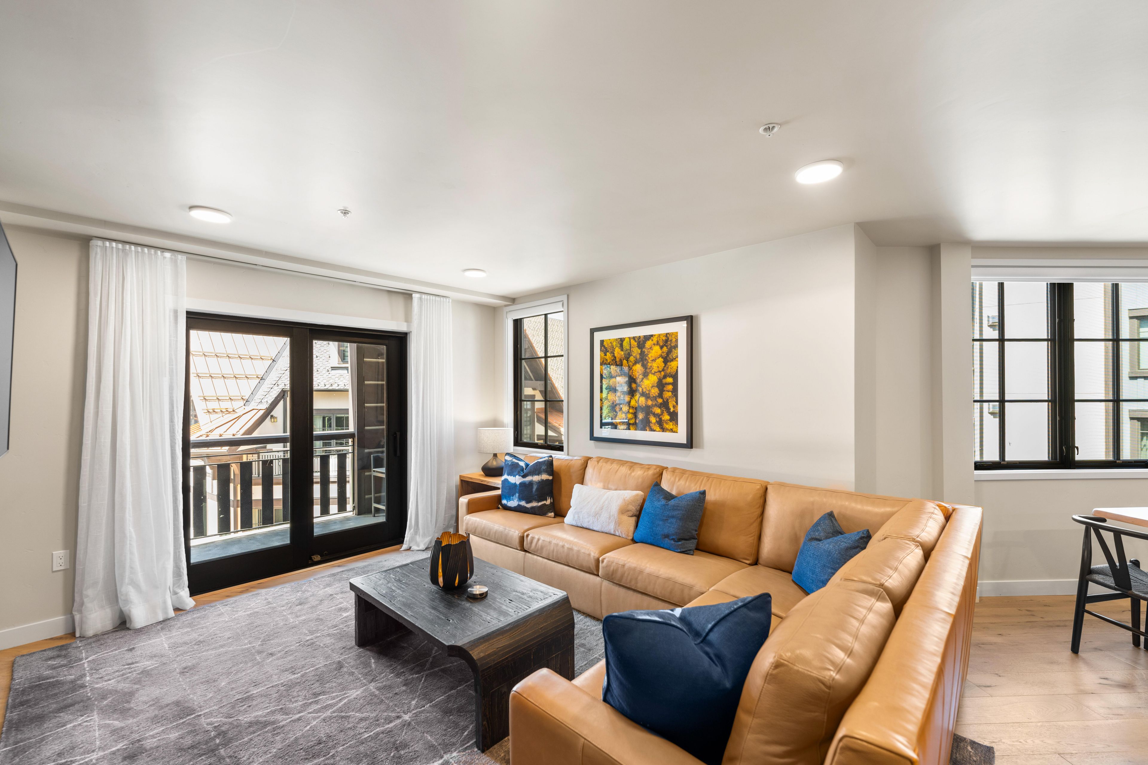 A modern living room with a leather sofa, a coffee table, and a large window with a view of the city.