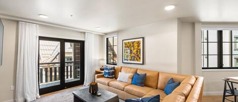 A modern living room with a leather sofa, a coffee table, and a large window with a view of the city.