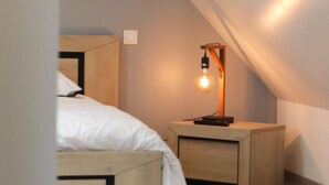 A bedroom with a wooden bed, a nightstand with a lamp, and a sloped ceiling. - Cozy Cottage for 2 with Terrace and WIFI in Normandy (Saint-Quentin-les-Chardonnets)