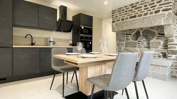 Una cocina moderna con armarios oscuros, una chimenea de piedra y un comedor con sillas grises y una mesa de madera.