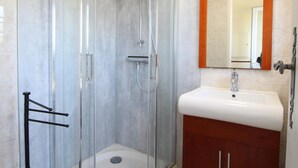 Une salle de bain avec une douche à parois de verre, un lavabo blanc et un meuble en bois.