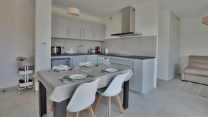Eine moderne Küche mit weißen Schränken, einem Esstisch für vier Personen und einem Sofa im angrenzenden Wohnbereich.