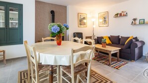 Un coin repas avec une table ronde, des chaises et un vase de fleurs. On aperçoit un canapé et une lampe au fond.