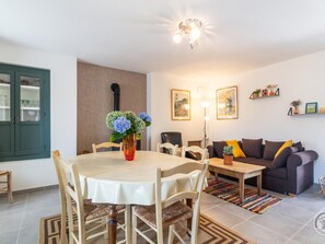 Ein Essbereich mit einem runden Tisch, Stühlen und einer Blumenvase. Im Hintergrund befindet sich eine Couch und eine Lampe.