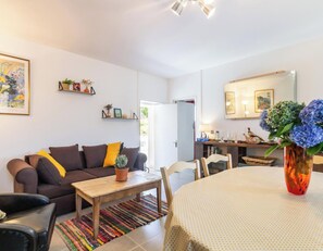 Un salon avec un canapé, une table en bois, une chaise, un tapis coloré et un vase rempli de fleurs.