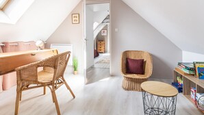 Une pièce mansardée chaleureuse, avec un bureau en bois, des chaises en osier, une petite table et une bibliothèque.