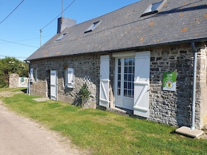 A stone building with white shutters, a green sign, and a clear sky.