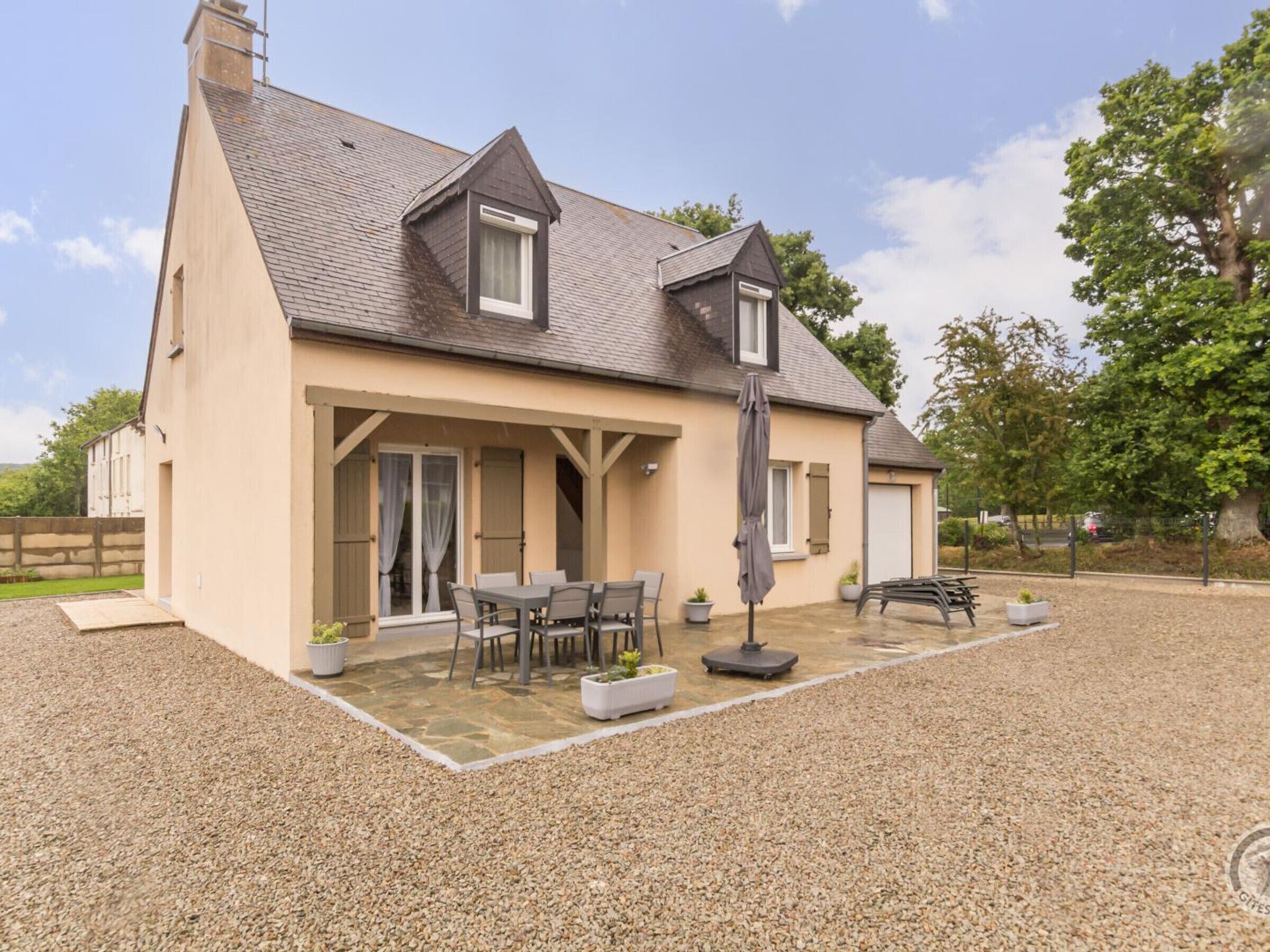 A two-story house with a covered patio, outdoor seating, and a gravel driveway.