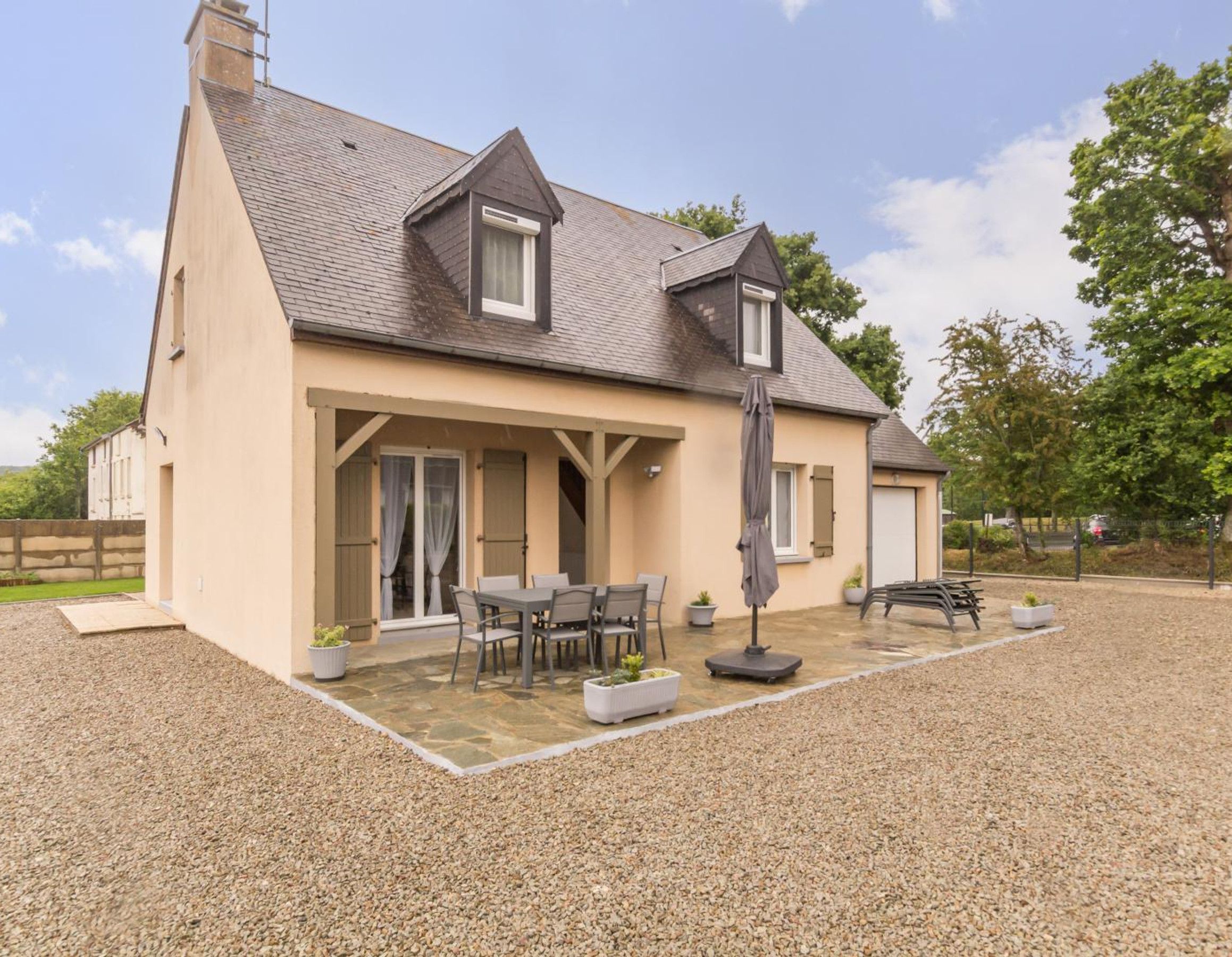 A two-story house with a covered patio, outdoor seating, and a gravel driveway.