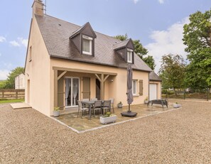 A two-story house with a covered patio, outdoor seating, and a gravel driveway.