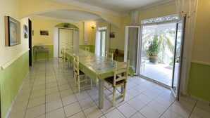 Een eetruimte met een lange tafel, stoelen en uitzicht op de omgeving door een glazen deur.