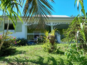A house with a porch, surrounded by lush greenery and flowering plants. - Creole Home for 6 in Saint-Leu with Bay View (Saint-Leu)
