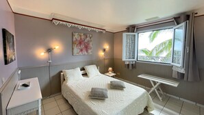 Een slaapkamer met een bed, nachtlampjes, een klein tafeltje, een raam met uitzicht en een schilderij aan de muur.