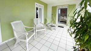 Een kamer met een groene wand, een witte betegelde vloer en witte meubels, waaronder twee stoelen en een klein tafeltje.