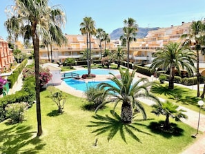 Un resort con piscina central, palmeras y montañas al fondo.