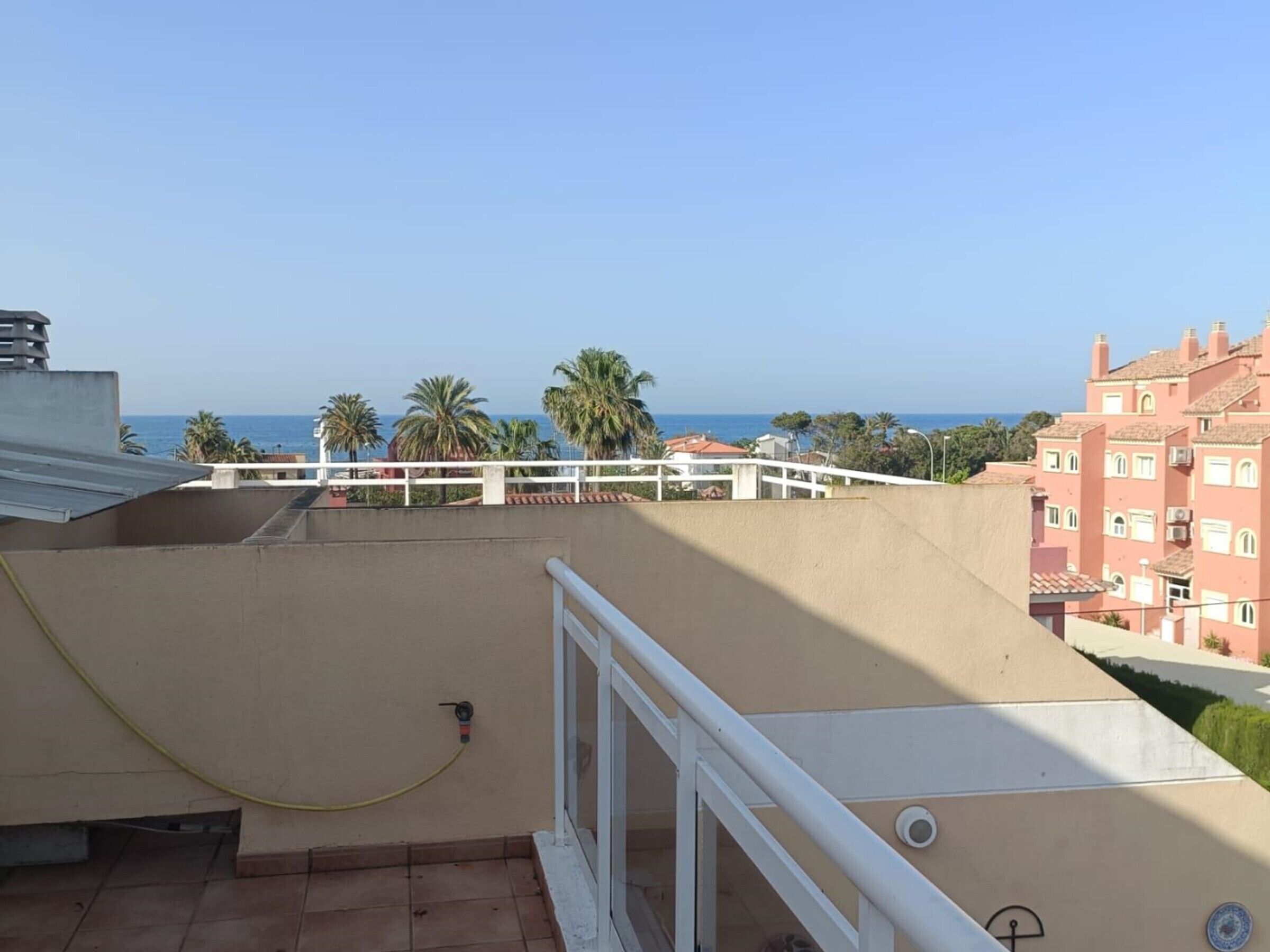 Un balcon avec vue sur la mer, les palmiers et les bâtiments voisins.
