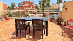 A terrace with a table and chairs, potted plants, and a view of a swimming pool and buildings. - Bright duplex with pool and parking in Denia (Denia)