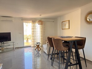 Un salon moderne doté d’un téléviseur à écran plat, d’une table basse en verre et d’un coin repas avec une table en bois et quatre chaises.