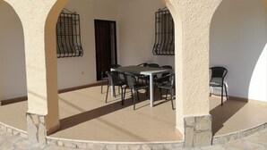 Eine Terrasse im Freien mit Tisch und Stühlen, umgeben von Steinmauern und Bögen.