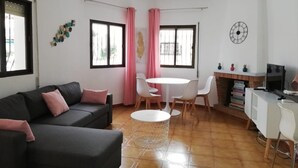 Ein Wohnzimmer mit Sofa, einem Esstisch mit Stühlen und einer Küchenzeile mit Herd.