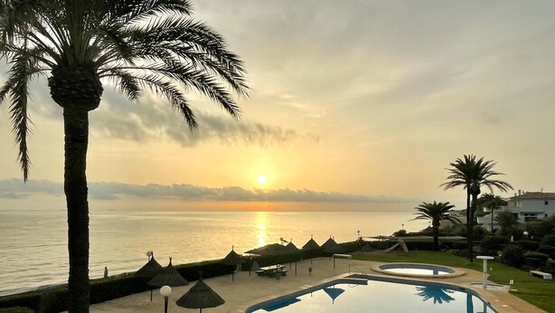 Ein Poolbereich mit Sonnenuntergangsblick, Palmen und einem Strand im Hintergrund.