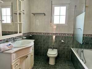 A bathroom with a sink, toilet, and bathtub, featuring a mirror, towel, and decorative tiles. - Cozy Villa in Els Poblets (Denia)