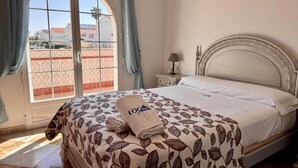 Habitación de hotel con cama, mesita de noche, lámpara y vistas a través de una ventana.
