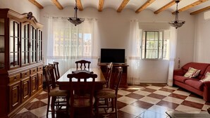 Un comedor con suelo a cuadros, vigas de madera en el techo, una mesa con sillas, un armario y un televisor.