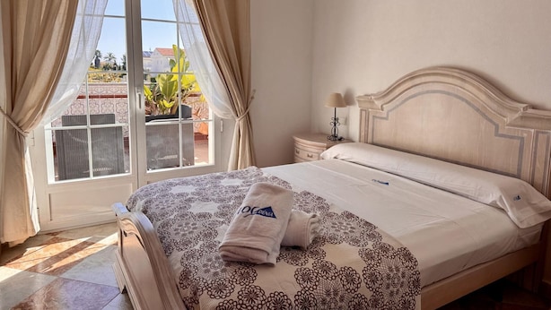 Un dormitorio con cama, una mesita de noche, una lámpara y vistas a través de una ventana.