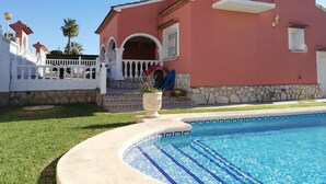 Un edificio rosa con piscina, balcón blanco y escalones de piedra.