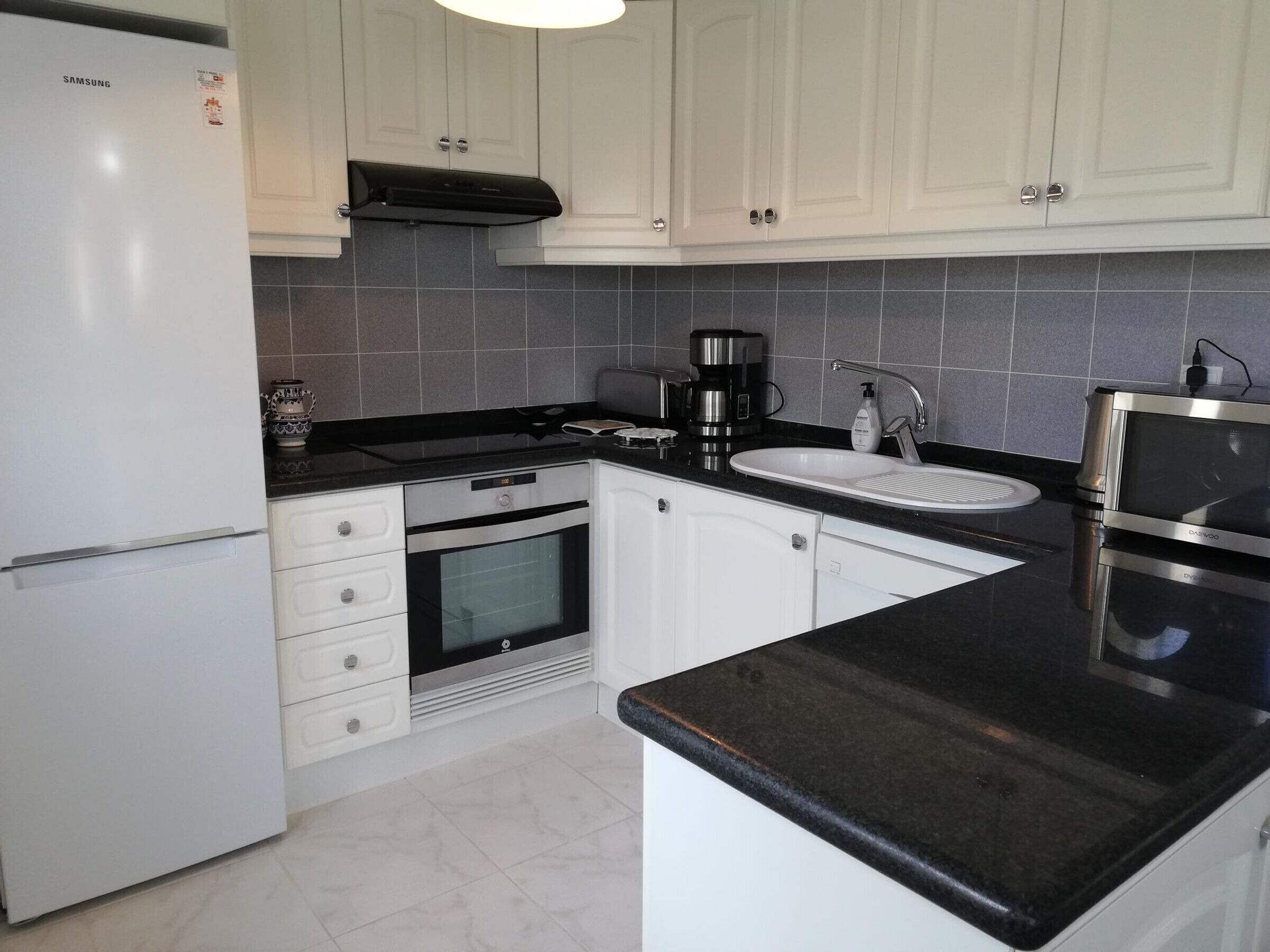 A modern kitchen with white cabinets, a built-in oven, a coffee maker, and a microwave.