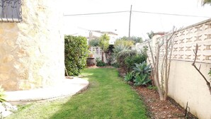 Un estrecho y cuidado sendero de jardín, con un muro de piedra a un lado y una cerca al otro, que conduce a un edificio con techo de tejas.