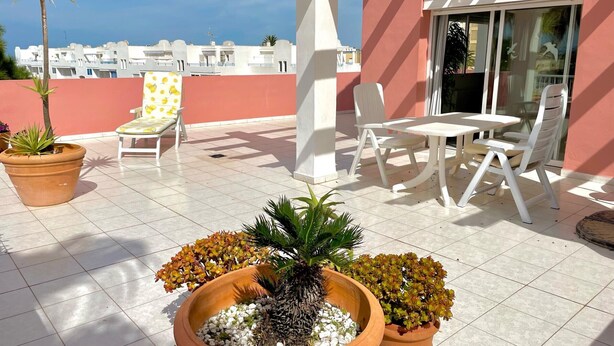 A terrace with potted plants, a white chair, a table, and a view of buildings in the background. - Penthouse in Denia with air conditioning and private parking (Denia)