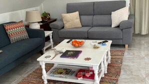 A living room with a grey sofa, a blue sofa, a white coffee table with magazines and a bowl of oranges, and a patterned rug. - Penthouse in Denia with air conditioning and private parking (Denia)