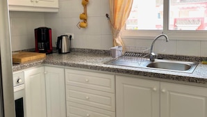 A kitchen with white cabinets, a granite countertop, a coffee maker, a kettle, a dish rack, and a window with curtains. - Penthouse in Denia with air conditioning and private parking (Denia)