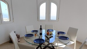 A dining area with a glass table surrounded by white chairs, a bottle of wine, and blue plates. - Spacious villa in El Ràfol d'Almúnia (El Ràfol d'Almúnia)