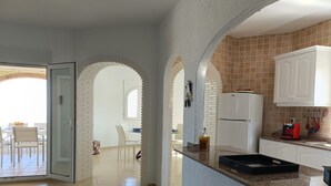 A modern kitchen with white cabinets, a granite countertop, and a built-in oven. There is a dining area with a table and chairs visible through an open door. - Spacious villa in El Ràfol d'Almúnia (El Ràfol d'Almúnia)