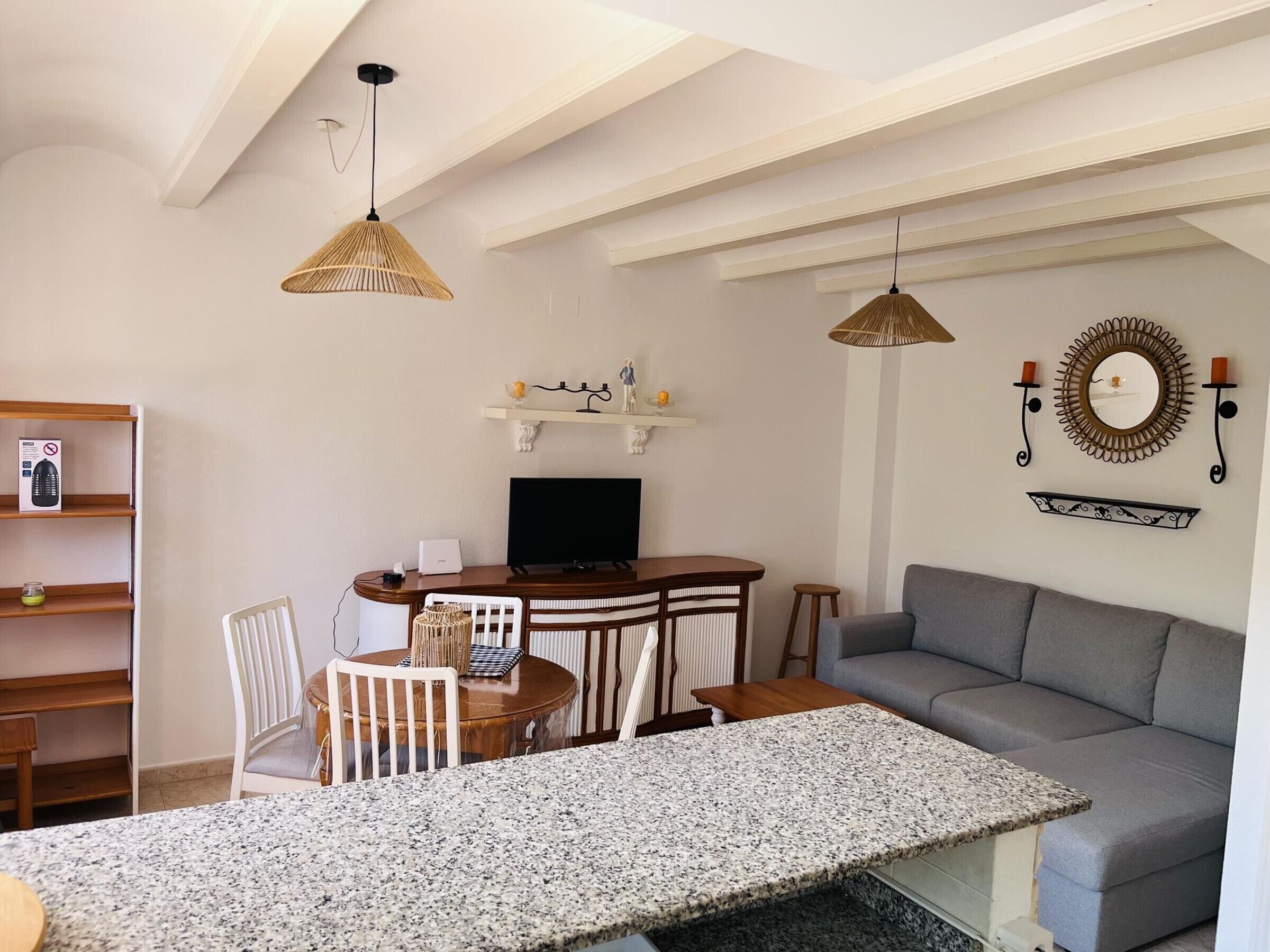 A modern living room with a dining area, a grey sofa, a TV, and decorative wall elements.