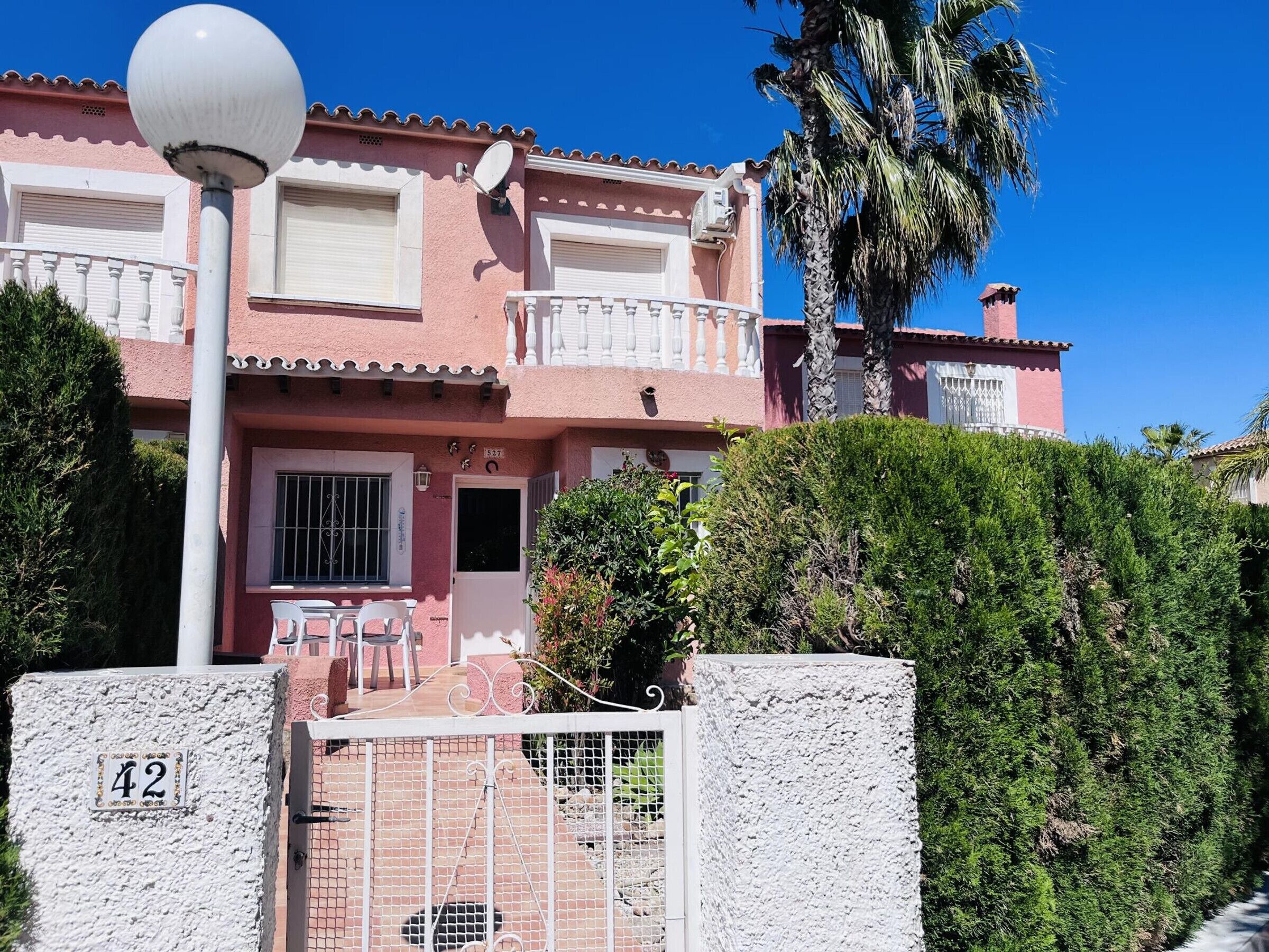 A pink villa with a balcony, a gate, and a number 42 sign.