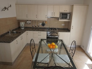 A compact kitchen with a granite countertop, a gas stove, a microwave, and a dining table with four chairs.