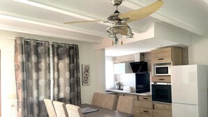 A compact kitchen with a microwave, oven, and a white refrigerator. There is a dining table with four chairs and a ceiling fan above. - Cozy 2-bedroom bungalow in Els Poblets with Wi-Fi and parking (Denia)