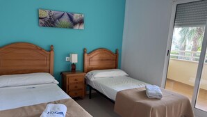 Habitación de hotel con dos camas, una mesita de noche, una lámpara, un cuadro en la pared y vistas a través de una puerta corrediza.