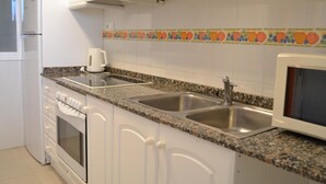 Una cocina con armarios blancos, encimera de granito, lavaplatos doble, cafetera y microondas.