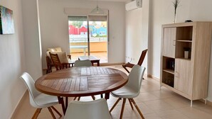 Comedor con una mesa redonda de madera, sillas blancas, un armario de madera y vistas a través de un ventanal.