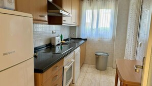 A compact kitchen with wooden cabinets, a built-in oven, a sink, and a trash bin. - Charming 3-bedroom apartment with terrace and garden access in Denia (Denia)