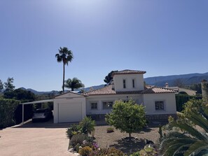 A two-story house with a tiled roof, a garage, and a garden with various plants.