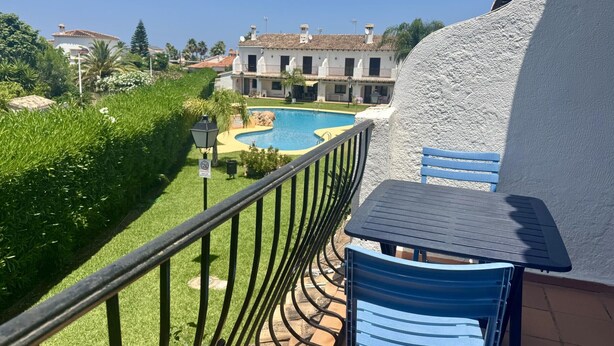 A balcony with a view of a swimming pool, a building with a white facade, and a blue chair. - Cozy Townhouse in Quiet Area (Denia)