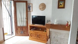 A living room with a television on a wooden stand, a fireplace, and a door with a curtain. - Cozy Townhouse in Quiet Area (Denia)